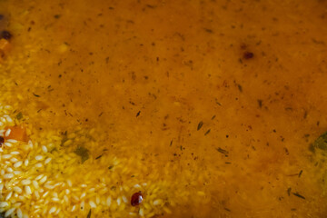 A close-up, high-angle shot of rice, spices, and other ingredients submerged in a rich broth during...