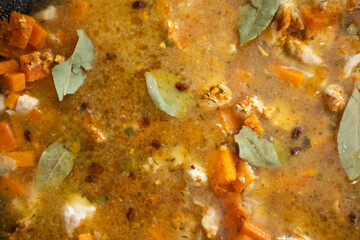 A close-up shot of cooked chicken, carrots, and onions mixed with spices, raisins, and bay leaves in a pan. This image captures the rich, colorful, and aromatic mixture that forms the base of Plov. Id