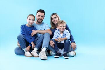 Happy parents and their children sitting on light blue background. Family