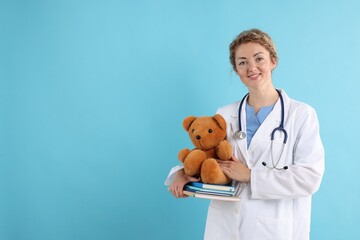 Pediatrician with toy bear and notebooks on light blue background. Space for text