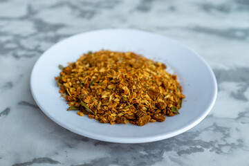 A pile of golden-brown spices, a key ingredient for Plov, is presented on a small white plate against a marble background. The mix of textures and vibrant colors adds visual interest. Perfect for food