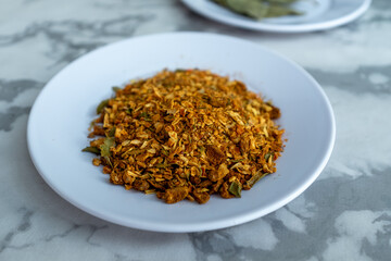 A pile of golden-brown spices, a key ingredient for Plov, is presented on a small white plate against a marble background. The mix of textures and vibrant colors adds visual interest. Perfect for food