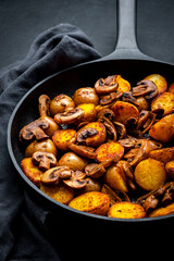 Baked golden potatoes with mushrooms in frying pan. Black background, top view