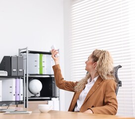 Woman using remote to control air conditioner in office