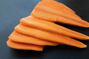 Bright orange, thick-cut carrot slices arranged on a dark surface. Fresh, raw, and prepped for...