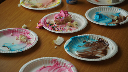Colorful paper plates with  food remnants lie scattered on a wooden table, hinting at a recently finished celebration. AI generated.
