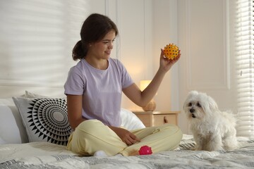 Happy teenage girl playing with cute Maltese dog on bed at home