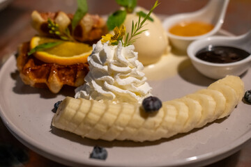 Waffle with vanilla ice cream served with sliced banana , whipped cream and sauce.