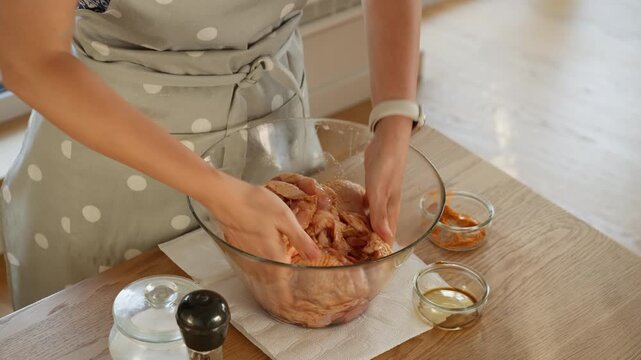 A woman's hands massage a savory marinade into raw chicken thighs. The process of coating poultry with spices and sauce ensures a tender, juicy, and flavorful meal for a homemade recipe.