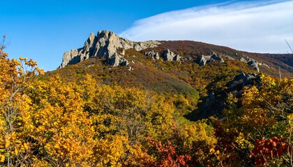 Obraz premium A vibrant autumn scene showcases a mountain range with colorful foliage and rocky peaks against a clear sky.