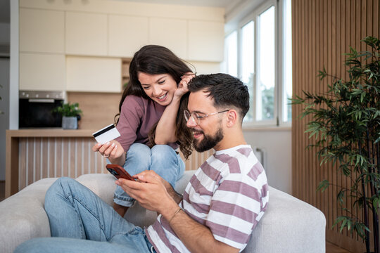 Happy couple shopping online using credit card and smartphone at home - Powered by Adobe