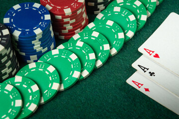 An exciting game of poker, brightly coloured chips are laid out around a winning hand of aces on a green felt table. The atmosphere heats up as the tension builds