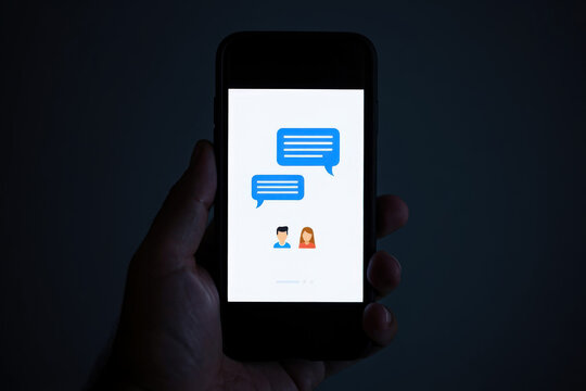 Illuminated Smartphone Displaying a Messaging Interface with Chat Bubbles and User Avatars, Held in Hand Against a Dark Backdrop, Representing Digital Communication and Social Interaction - Powered by Adobe
