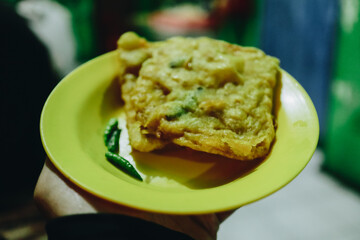 Deliciously Crispy Fried Snack Served on a Bright Yellow Plate with Green Chilis