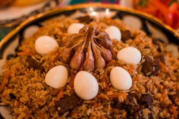 Traditional Uzbek rice dish pilaf, featuring tender meat, aromatic spices, and garnished with quail eggs and garlic, showcasing rich culinary heritage and vibrant presentation. Copy space, menu