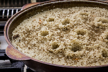Traditional Uzbek rice dish pilaf, is being prepared in a large pot, showcasing aromatic spices and...