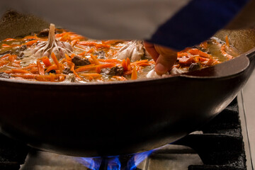 Cooking traditional Uzbek dish pilaf, in a large pot, featuring vibrant carrots and tender meat,...