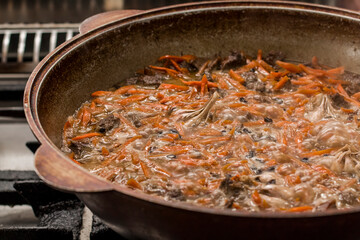 Traditional Uzbek dish pilaf, simmering in a large pot, featuring vibrant carrots and tender meat,...