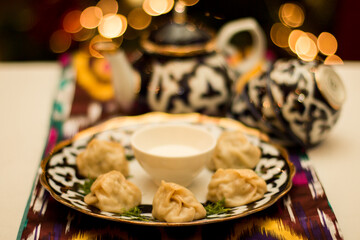 Traditional Manti Uzbek dumplings served on a decorative plate with yogurt dip, surrounded by...