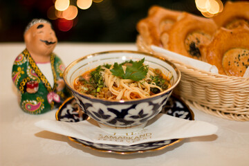 Traditional Uzbek noodle dish served in ornate bowl with fresh herbs, accompanied by freshly baked...