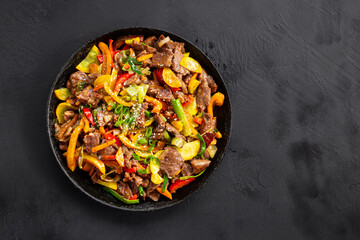 Beef stir fry in a frying pan top view, Asian meat with vegetables on a black background