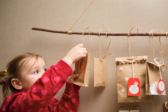 child looks at the advent calendar. Baby girl in a Christmas hat and pajamas takes first gift