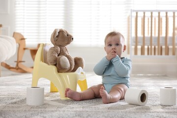 Cute little baby with rolls of toilet paper near potty on floor at home