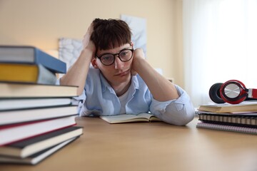 Tired student preparing for exam at table indoors