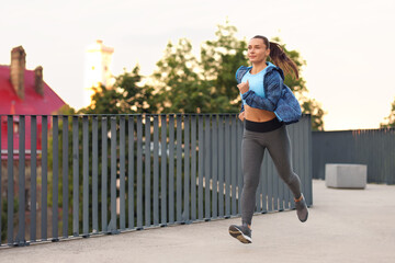Young woman in sportswear running outdoors, space for text
