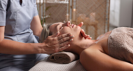 Beautiful woman receiving facial massage on couch in spa salon, closeup