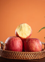 Fresh Red Fuji Apples in Wicker Basket Display Against Orange Background