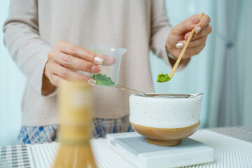 Asian woman preparing traditional Japanese matcha tea at home using bamboo tools, sifting matcha powder with care and precision.