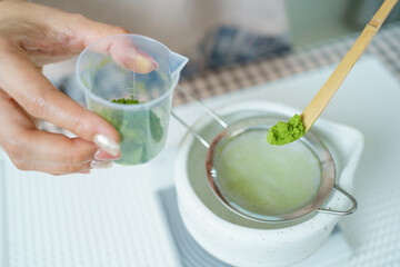 Asian woman preparing traditional Japanese matcha tea at home using bamboo tools, sifting matcha powder with care and precision.