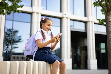 Schoolgirl with backpack using smartphone outside the school building.