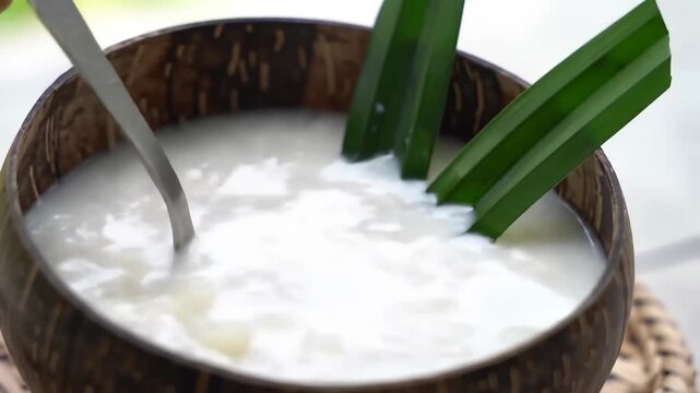 Sweet white soup being poured into a dark wooden bowl, top view