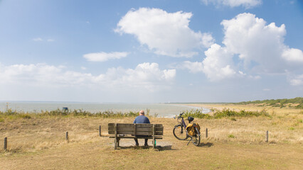 Obraz premium cycliste assis sur un banc face à la mer. senior, homme âgé profitant du paysage face à l'océan. Scène calme et tranquille en été
