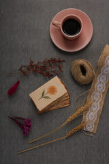 A flat lay of a pink coffee cup, a stack of torn paper with a hand-painted flower, a ball of twine,...