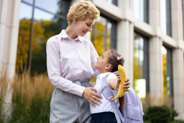 A mom and her daughter share a tender moment in a schoolyard, with the little girl holding a banana.