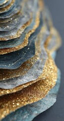 Close-up of layered, textured paper art.  Multi-toned, overlapping,  organic forms in shades of gold, blue-grey, and gray.  Glitter accents