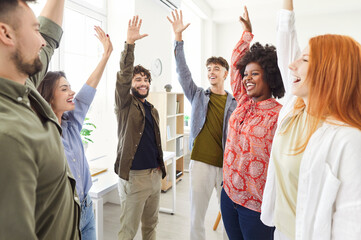Multinational team of business people in the office celebrates success by raising hands during a...