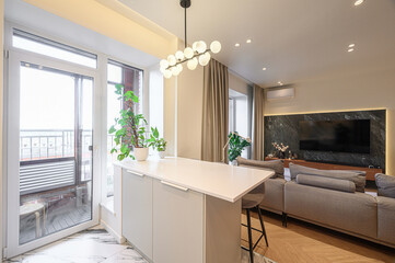 Bright, modern living room featuring a kitchen island, balcony access, a comfortable sofa, and...