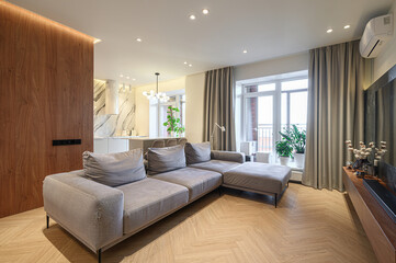 modern living room features a large gray sectional sofa, wooden floors, and a kitchen visible in...