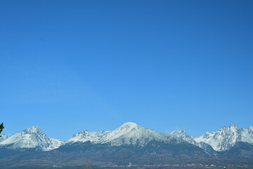 A distant view from the hill of the high peaks of snow-capped mountains High Tatra in spring