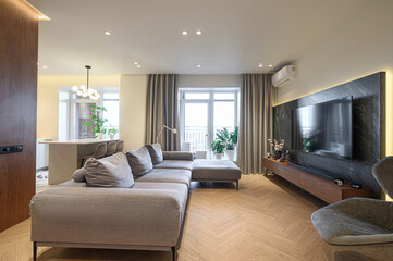 Cozy living room with a large grey sofa, herringbone floor, TV on a marble wall, and plants. A modern, bright interior design