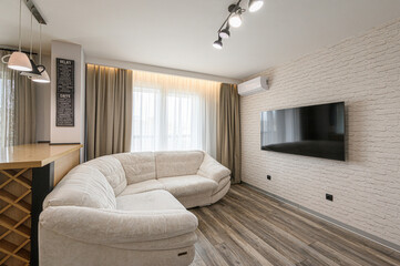 cozy living room with a curved white sofa, brick wall, TV, wooden floor, and soft lighting