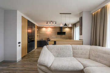 Modern open-concept living space. Features a beige sofa, wood floors, and a stylish kitchen with black and wood cabinets
