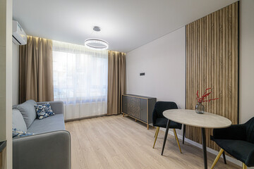 modern living space featuring a gray sofa, round table with black chairs, wooden wall panel, and...