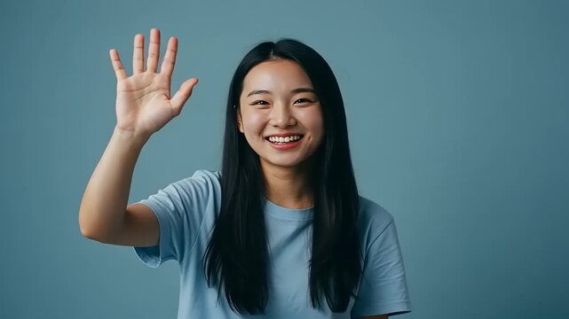 Young woman smiling and waving hello against a blue background, conveying friendliness and warmth - Powered by Adobe