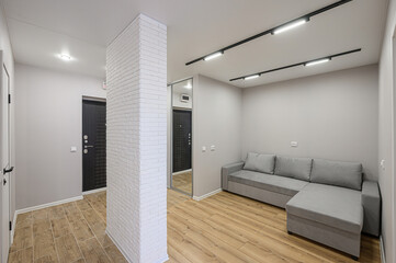 bright interior view features a gray sofa, wood flooring, and a white brick accent wall,...
