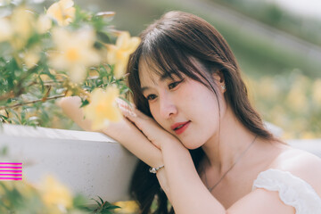 Serene contemplation: A delicate Asian woman rests peacefully beside vibrant yellow flowers,...